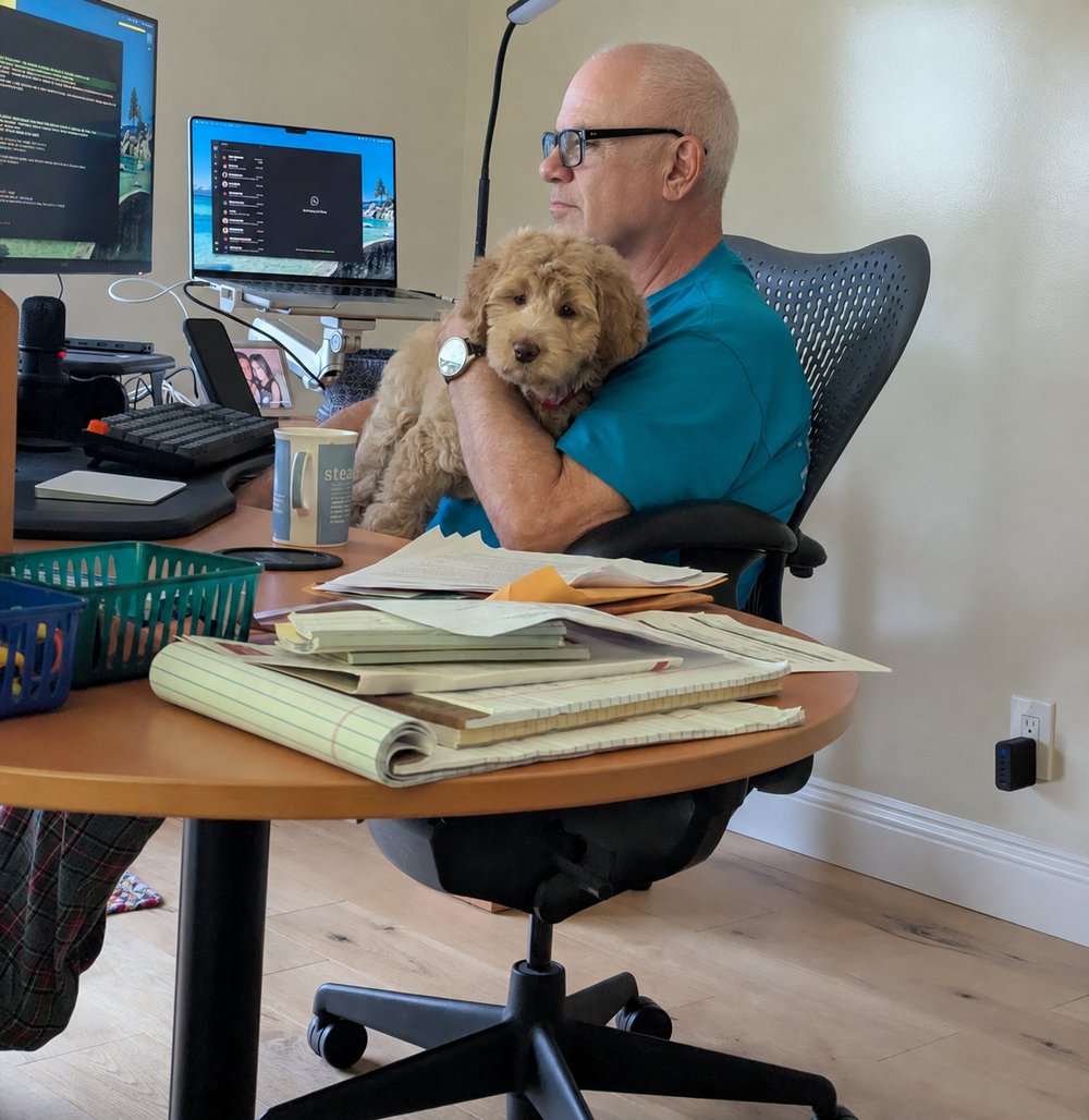 Simon Politakis at his desk in front of two monitors, holding his labradoodle puppy in his lap